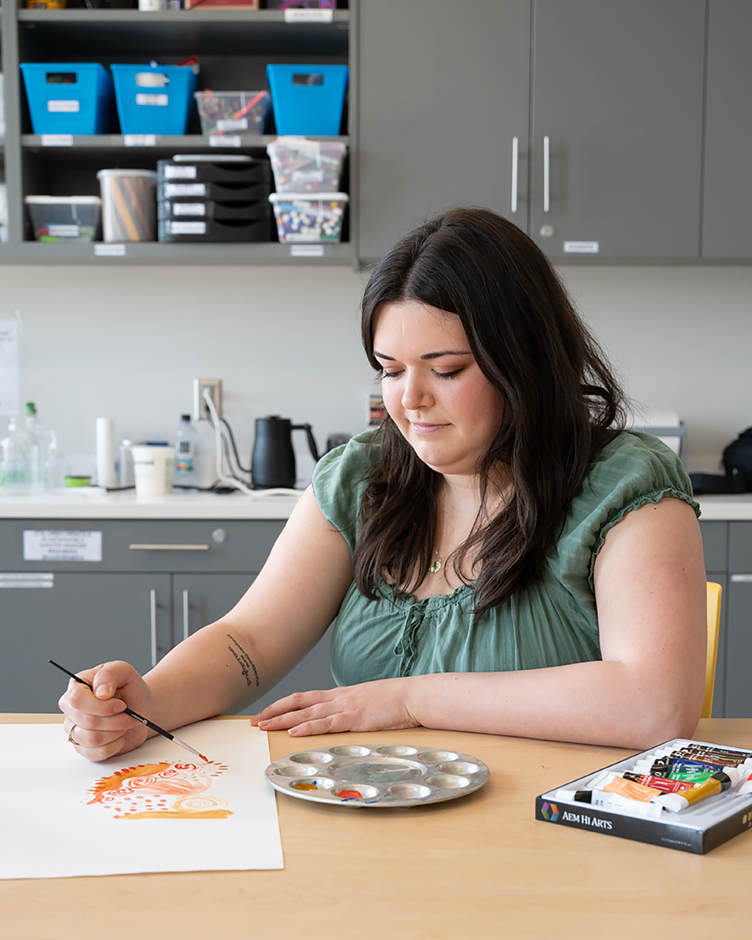 Morgan is seated at table in CAT studios, creating a watercolor artwork on white paper 